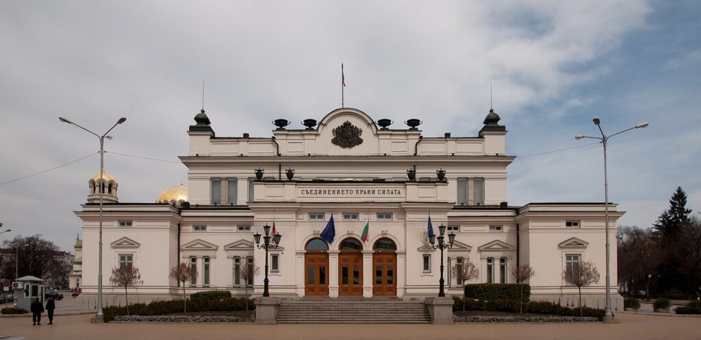 Пленарната зала на парламент с редове седалки и трибуна преди заседание